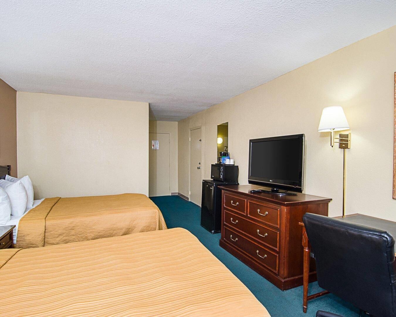 A hotel room with two beds, a TV, a dresser, and a lamp.