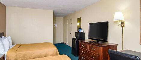 A hotel room with two beds, a TV, a dresser, and a lamp.