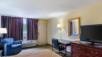 Ein Hotelzimmer mit Bett, Schreibtisch, Stuhl, Fernseher und einem Fenster mit Vorhängen.