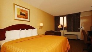 A hotel room with a large bed, a desk, a chair, and a window with curtains. - Quality Inn Shenandoah Valley (New Market)