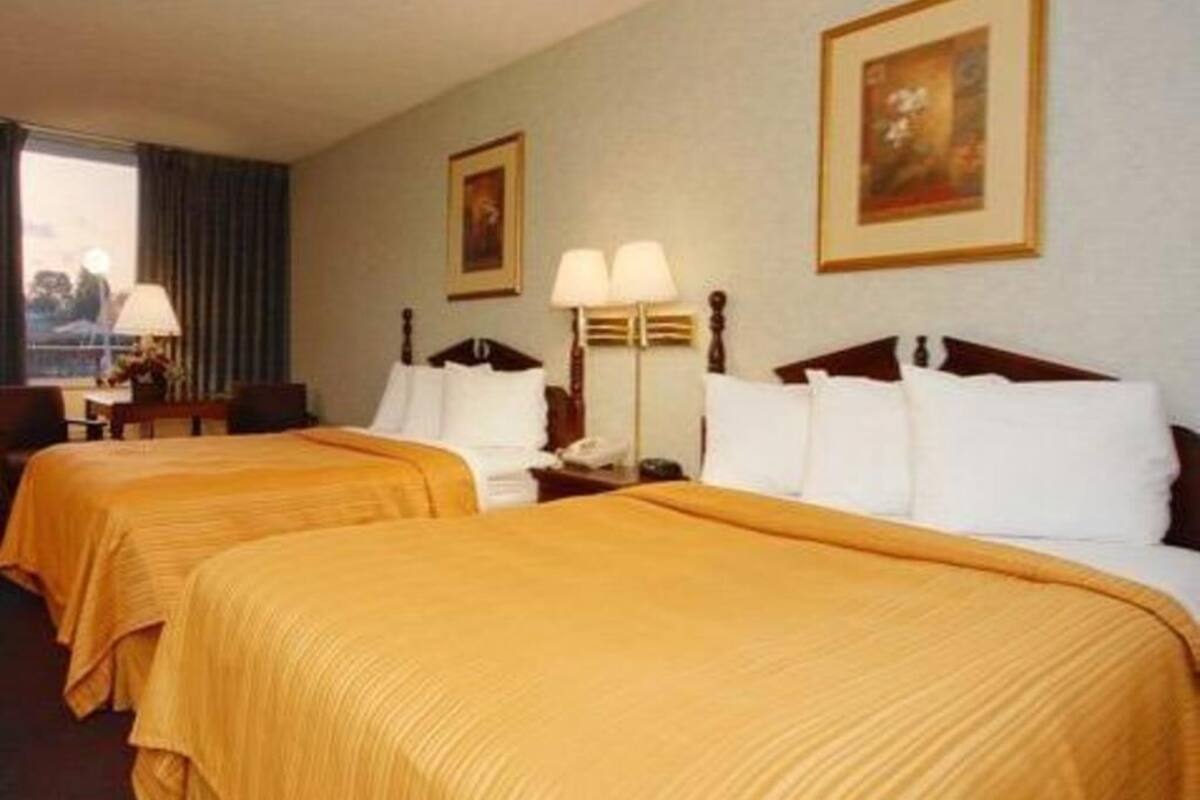 A hotel room with two beds, a desk, a lamp, and a painting on the wall.