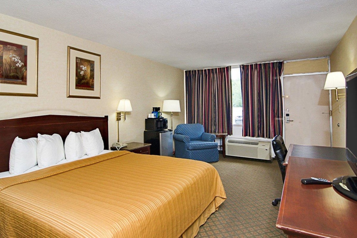 A hotel room with a bed, a desk, a chair, a television, and a window with curtains.
