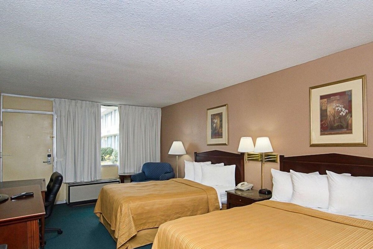 A hotel room with two beds, a desk, a chair, and a window with curtains.