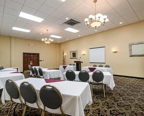 A conference room with tables, chairs, a projector screen, and an exit sign.