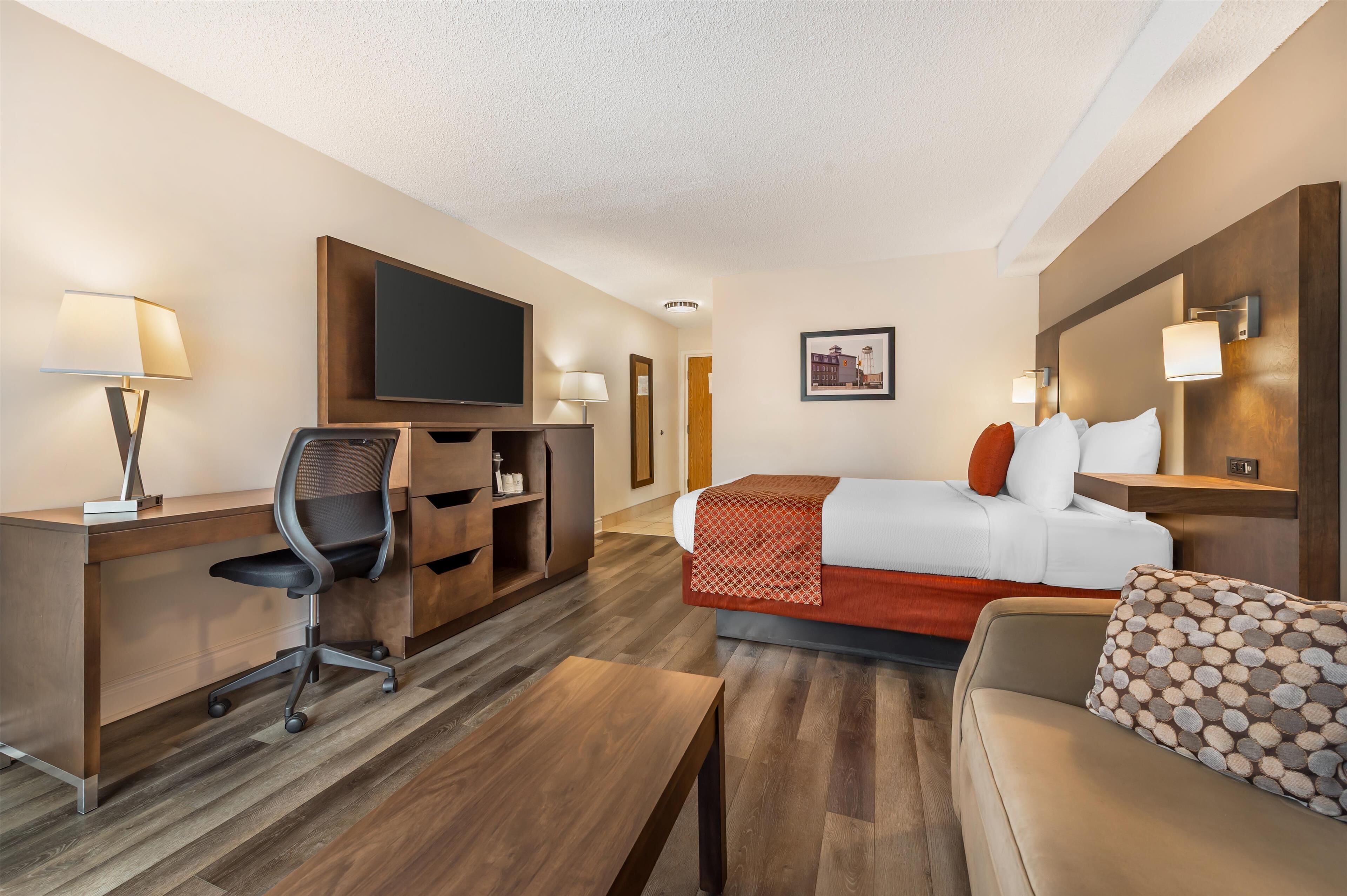 A hotel room with a bed, a desk, a chair, a TV, and a sofa.