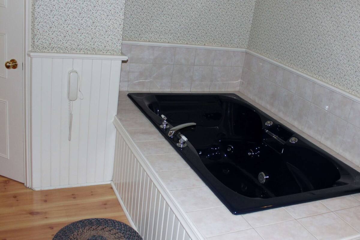 Een badkamer met een zwart bad, een witte radiator en een rieten mand met een rode kussentje.