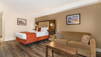 A hotel room with a bed, a sofa, a coffee table, and two framed pictures on the walls.