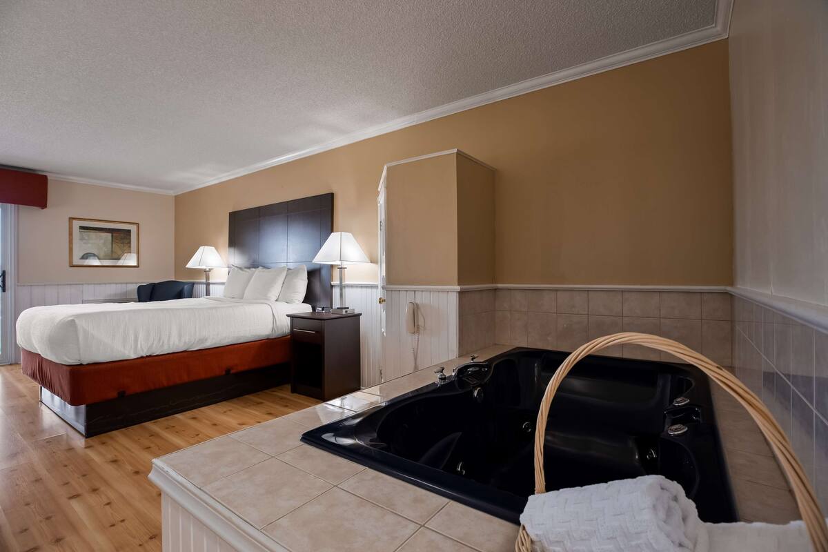 Een hotelkamer met een bed, nachtlampjes, een telefoon, een badkuip en een schilderij aan de muur.