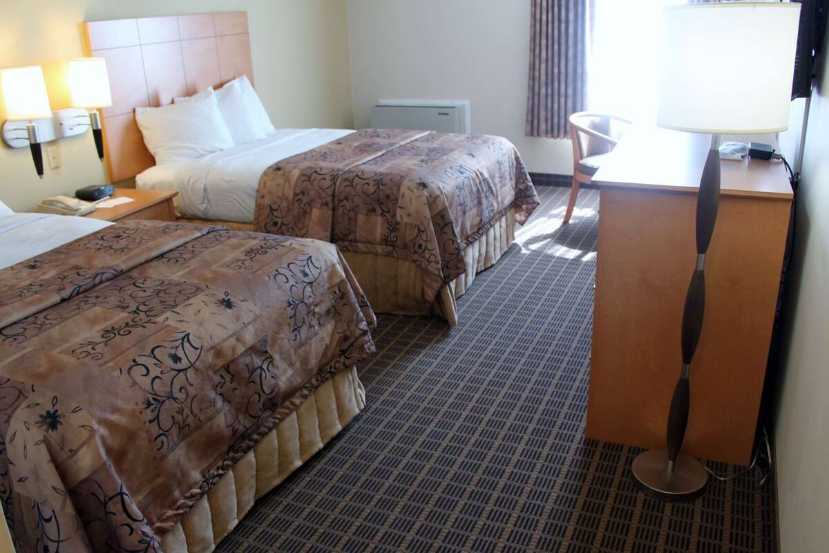 Een hotelkamer met twee bedden, een bureau, een stoel en een lamp.