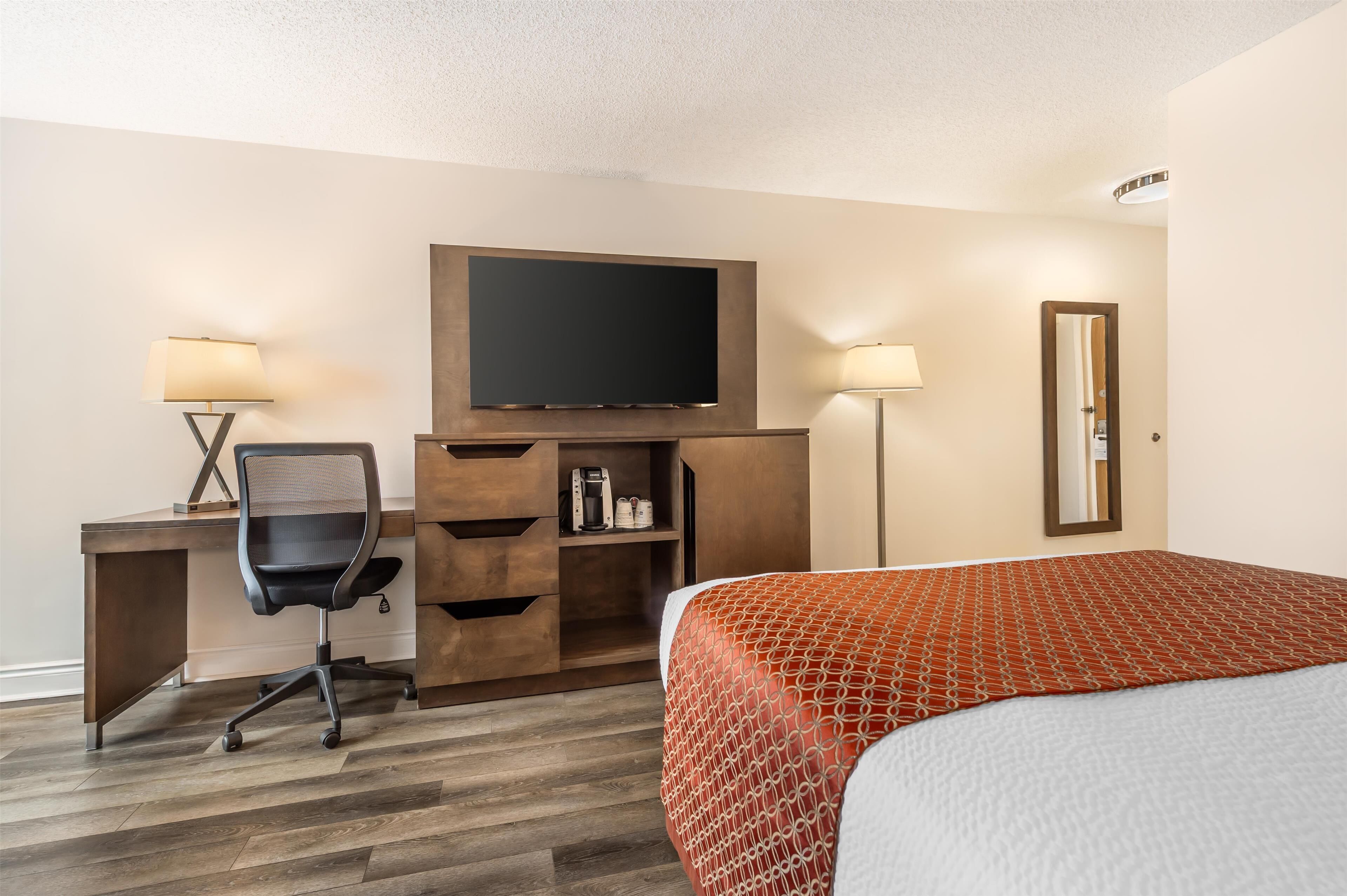 A hotel room with a bed, a desk with a chair, a television, and a mirror.
