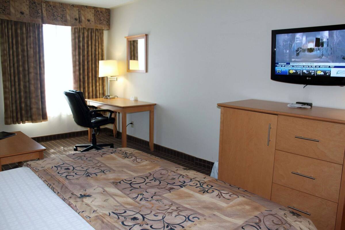 Een hotelkamer met een bed, bureau, stoel, televisie en een kledingkast.