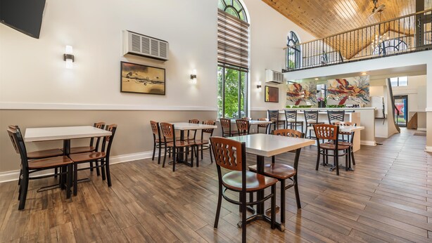 Un comedor amplio con varias mesas y sillas, un techo alto con vigas de madera y una escalera que conduce a un nivel superior.