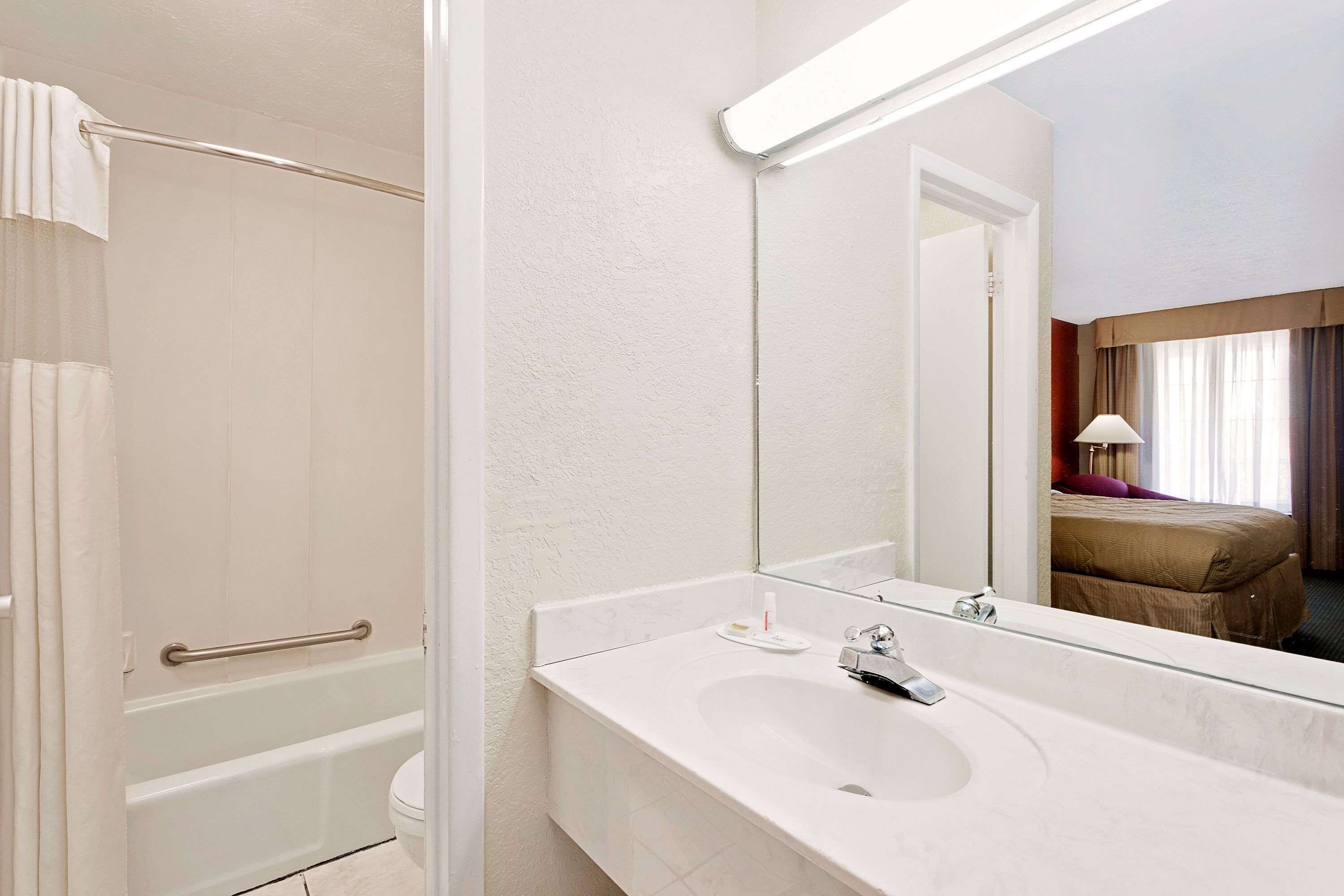 A hotel bathroom with a bathtub, a sink, and a mirror.