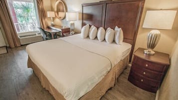 Habitación de hotel con una cama grande, un escritorio, una silla, una lámpara y una ventana con cortinas.