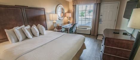 Habitación de hotel con una cama grande, un escritorio con lámpara, una cómoda y una ventana con cortinas.