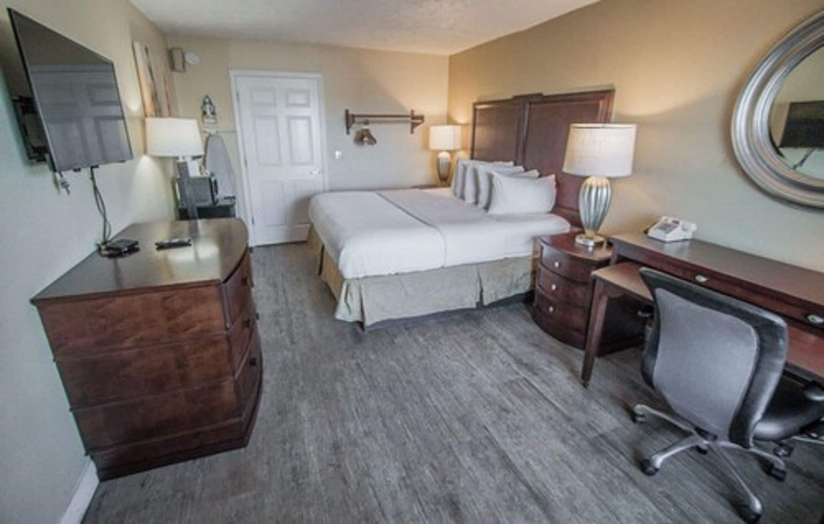 A hotel room with a bed, a desk, a chair, a dresser, and a television.