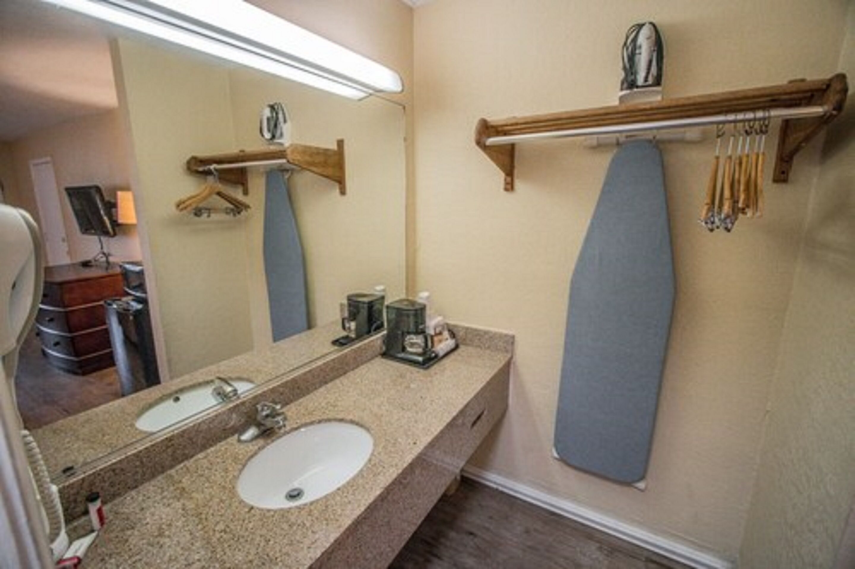 A bathroom with a granite countertop, two sinks, a large mirror, and a wooden ironing board.