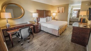 Ein Hotelzimmer mit Bett, Schreibtisch, Stuhl, Kommode und Spiegel.