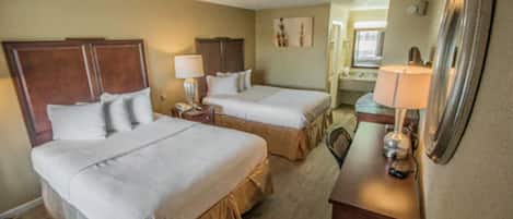 A hotel room with two beds, a desk with a lamp, and a mirror.