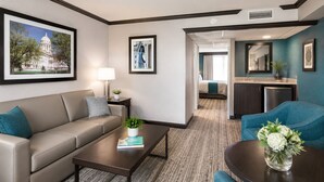 A hotel room with a sofa, a coffee table, a dining table with a vase of flowers, a kitchenette, and a bathroom visible through an open door. - Wyndham Garden Oklahoma City Conference Ctr/Airpt/Bricktown (Oklahoma City)