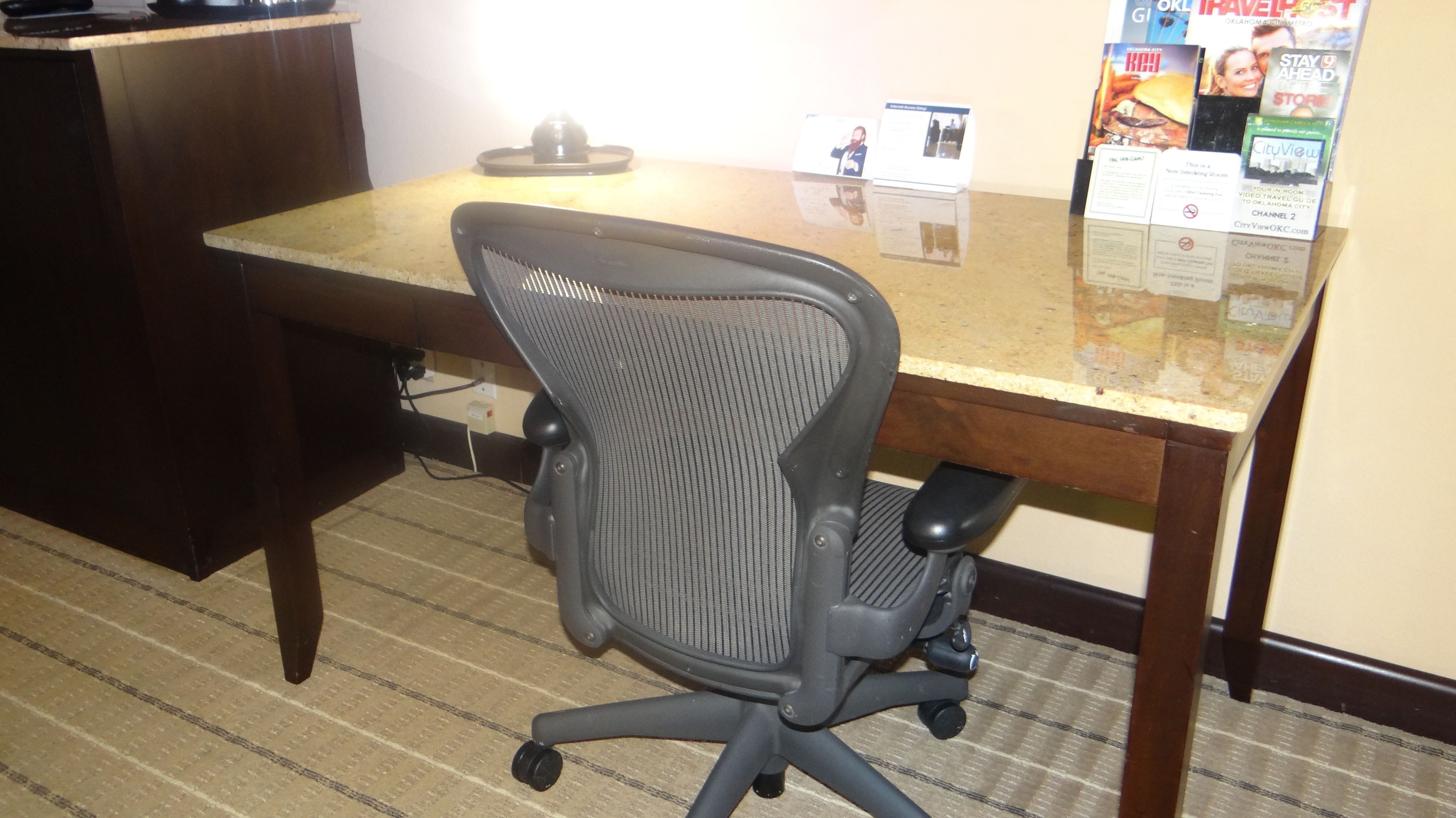 A conference room with a wooden desk, a black office chair, and a bulletin board with travel brochures.
