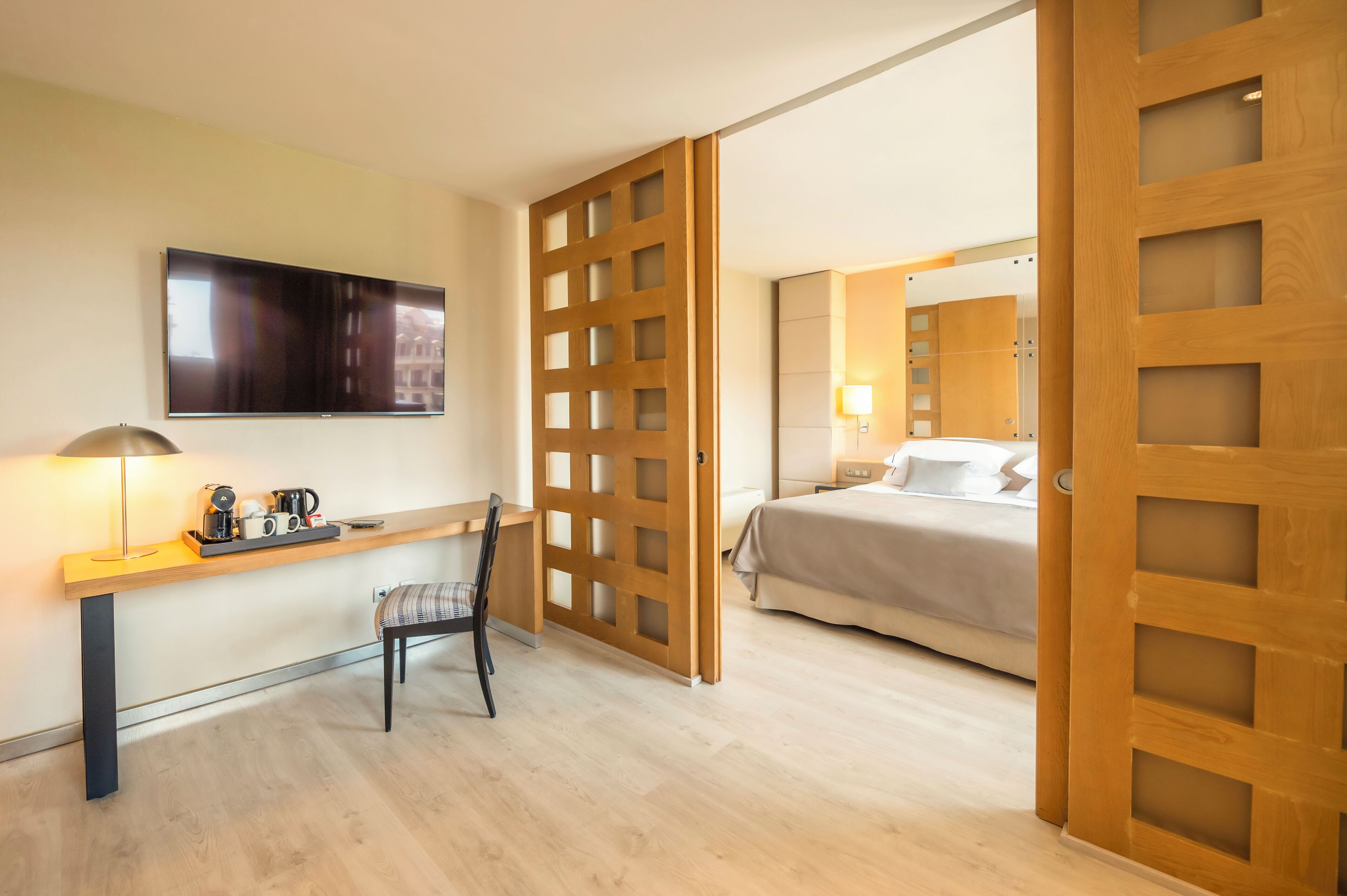 A hotel room with a desk, chair, bed, and a TV mounted on the wall.