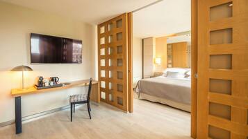 A hotel room with a desk, chair, bed, and a TV mounted on the wall.