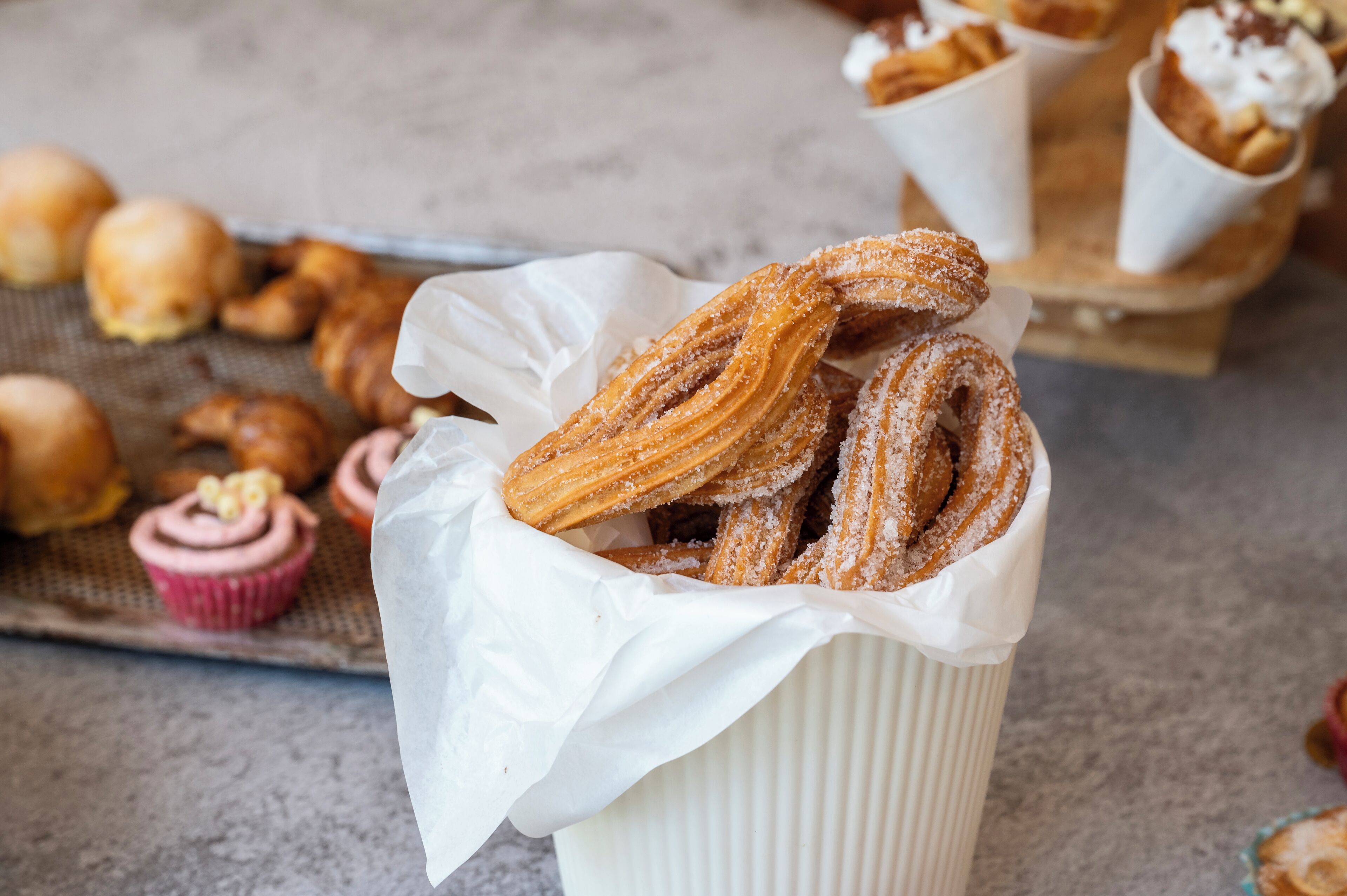 Een bak churros met suiker, een cupcake en andere gebakjes op een tafel.