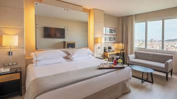 Habitación de hotel con una cama grande, un sofá, una mesita y una ventana con vista a la ciudad.