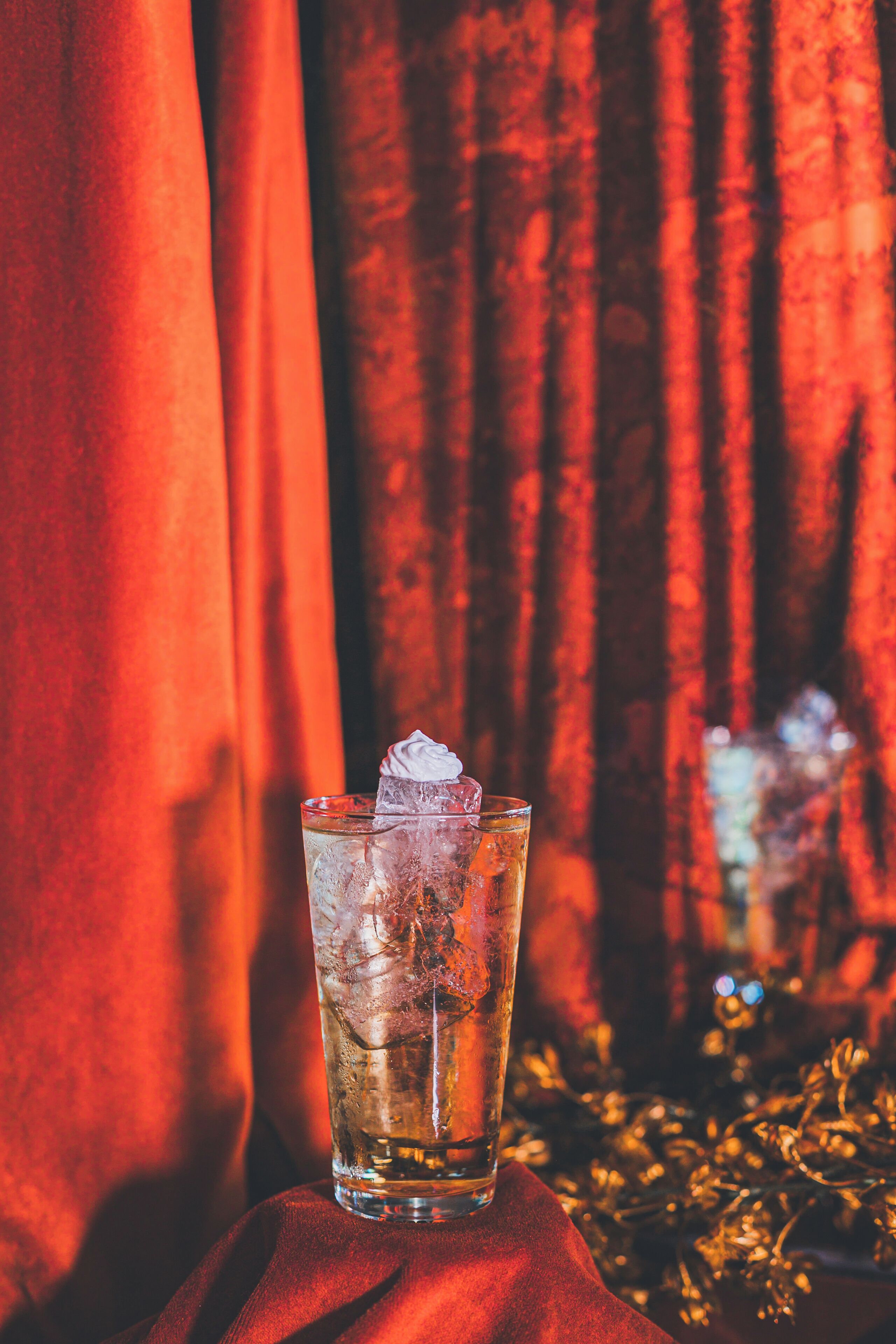 A glass of amber liquid with ice cubes on a table with a red cloth.