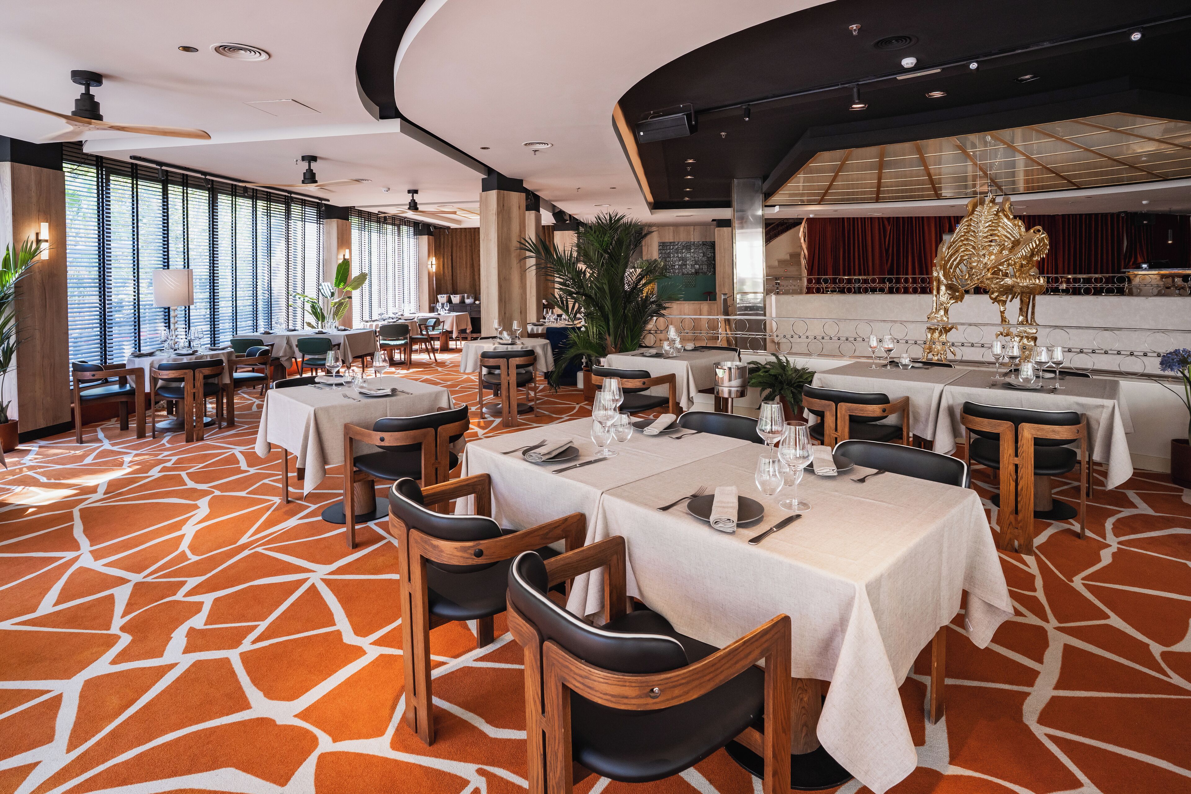 Un restaurant avec des tables dressées pour le service, une chaise dorée décorative et un sol à motifs.