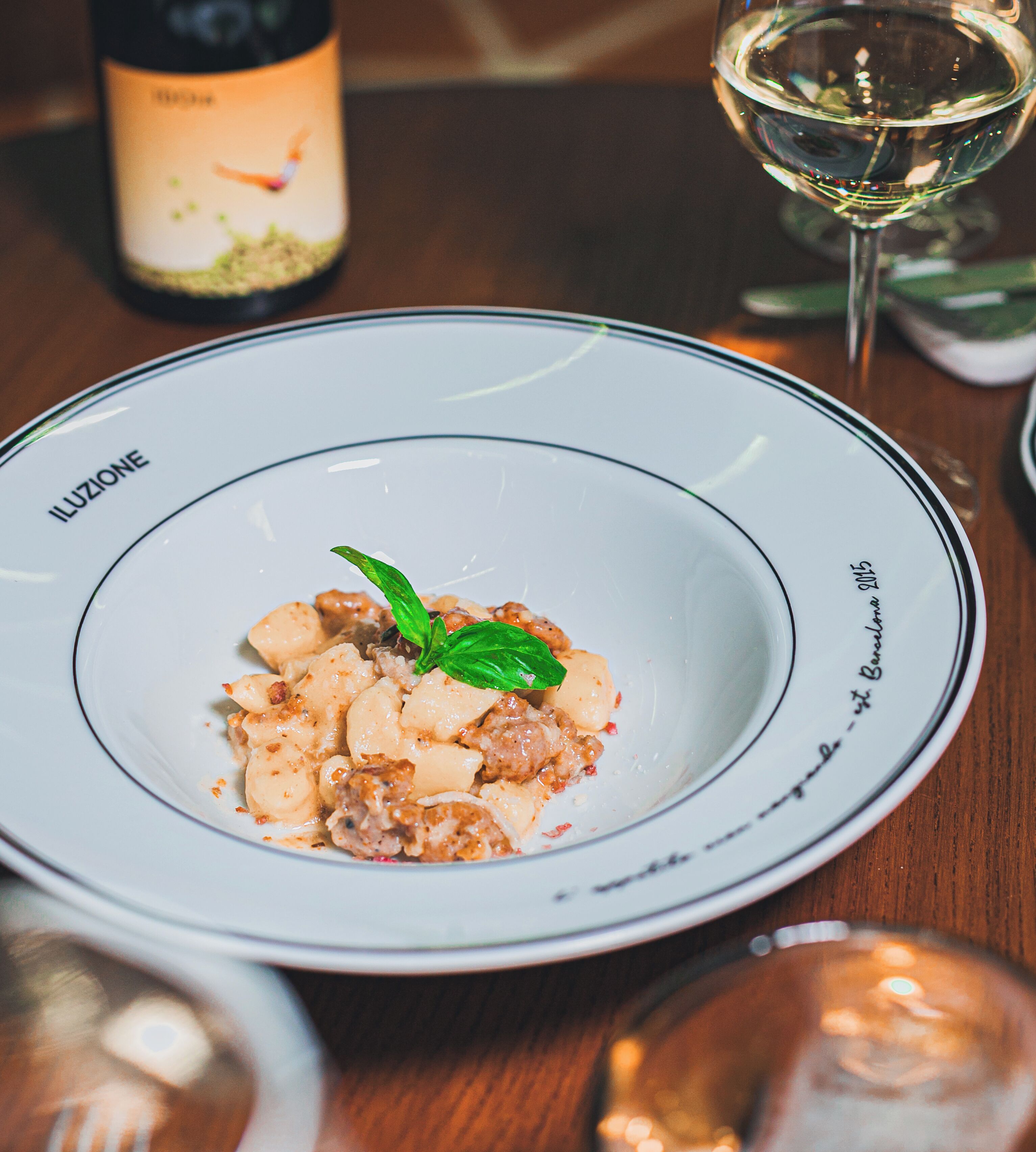 A plate of food with a basil garnish, a wine bottle, and a glass of white wine on a wooden table.