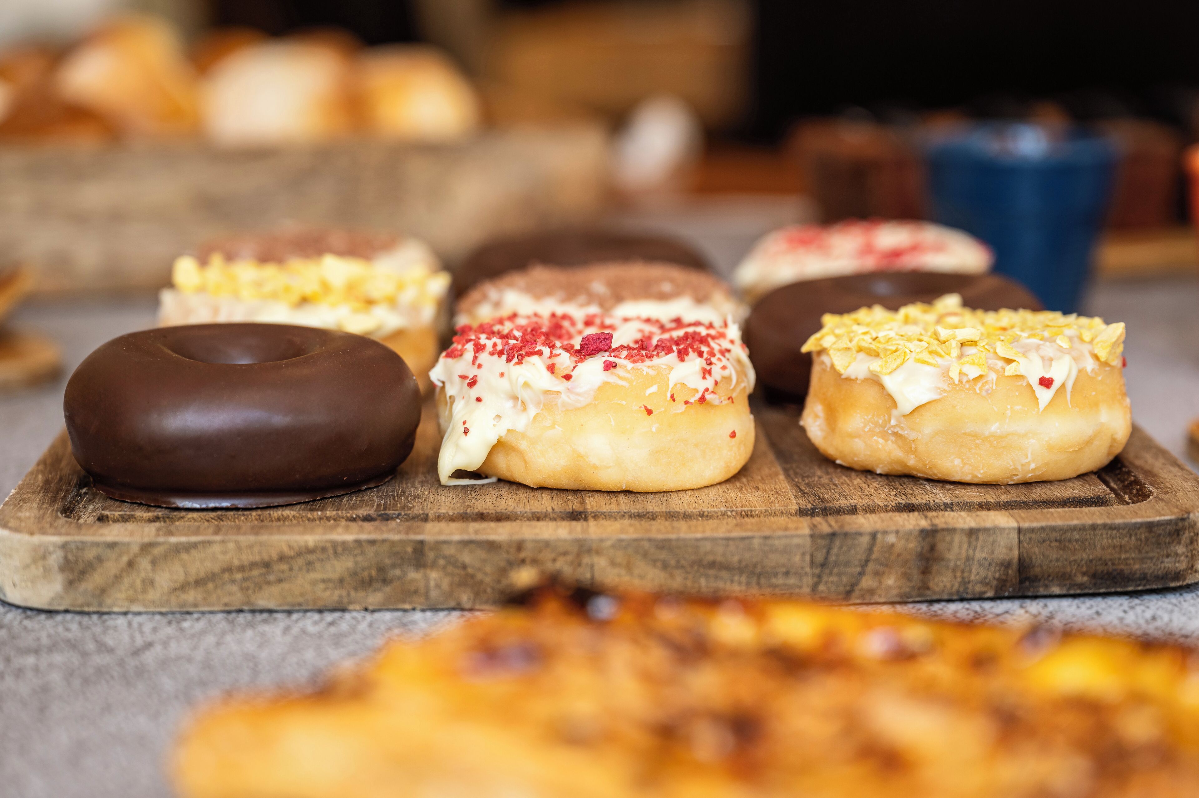Een houten plank met diverse donuts, waaronder chocolade- en roomgevulde varianten, gepresenteerd op een aanrecht.