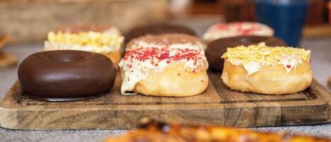 Een houten plank met diverse donuts, waaronder chocolade- en roomgevulde varianten, gepresenteerd op een aanrecht.