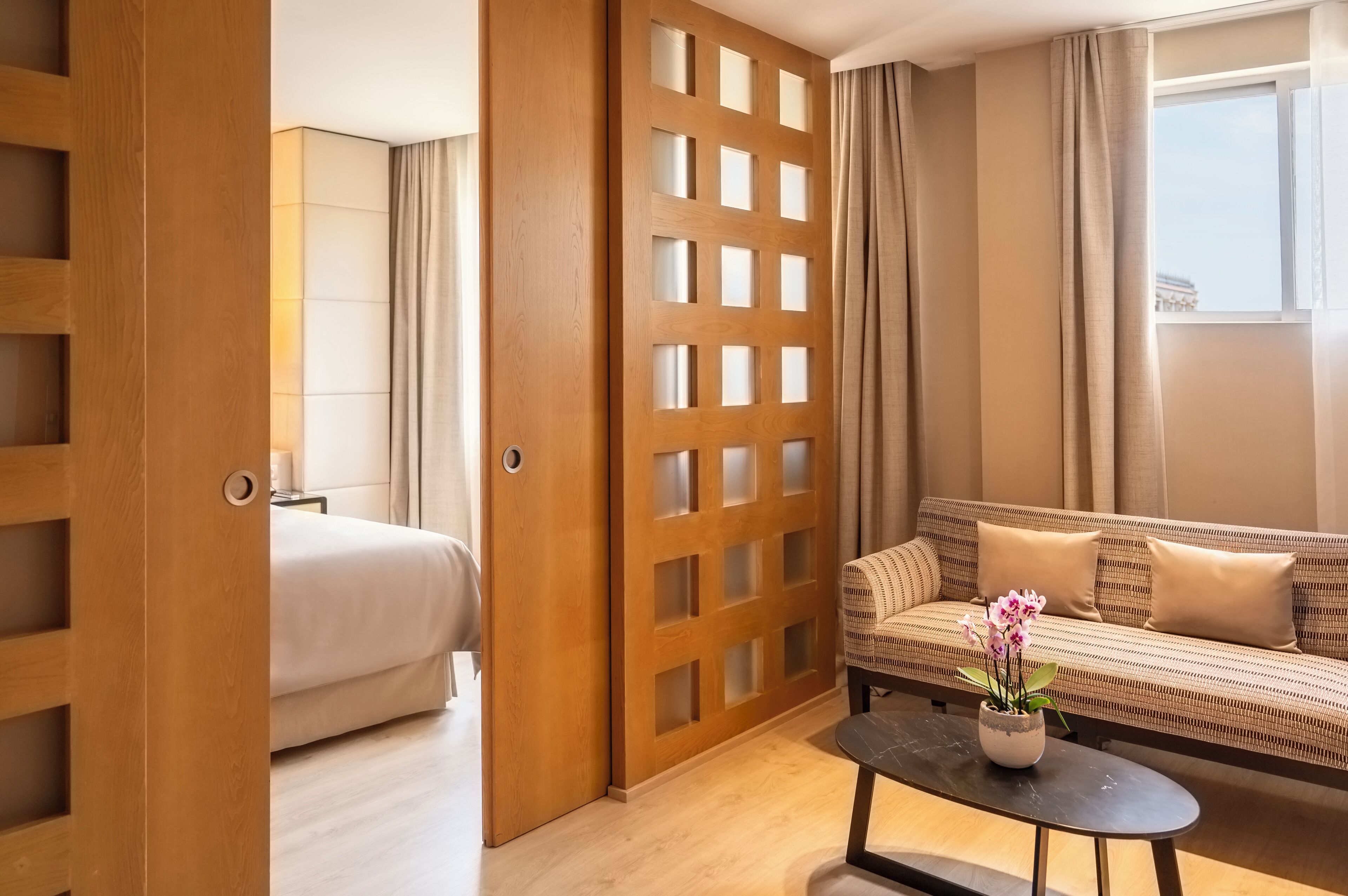 Une chambre d’hôtel avec un lit, un canapé, une table basse avec une plante et une cloison en bois.