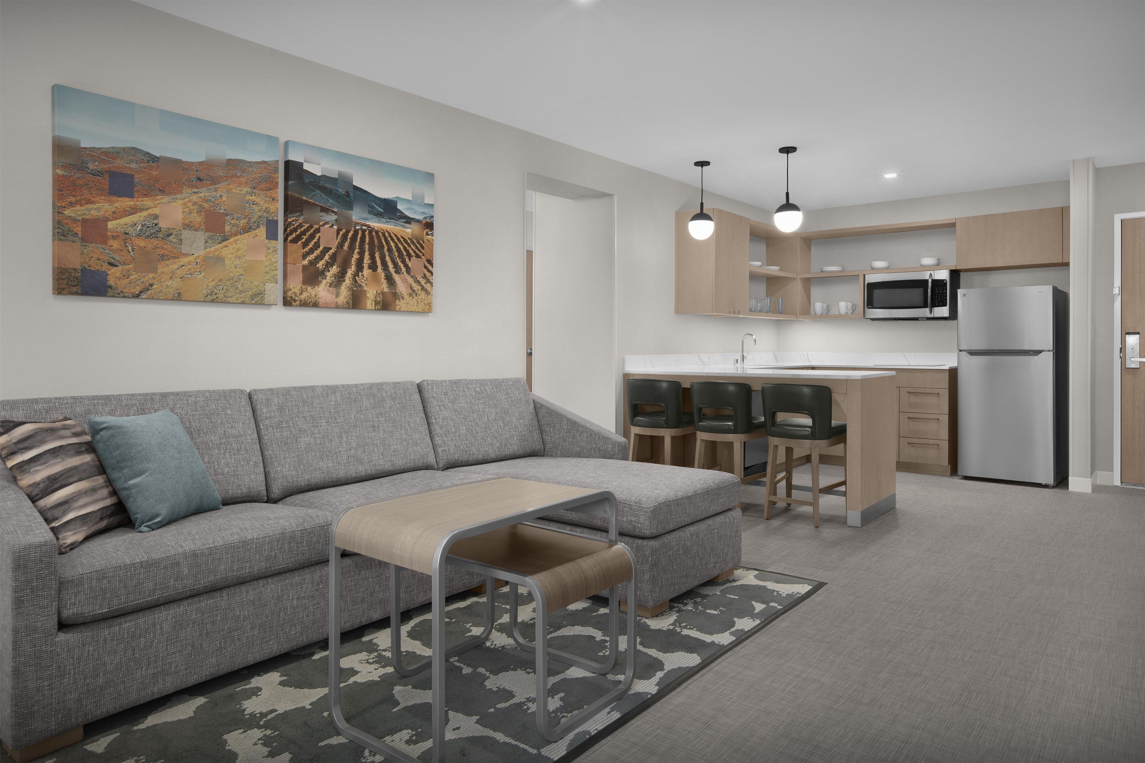 Una sala de estar moderna con un sofá gris, una mesita y una cocina con microondas y armarios.