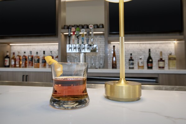 Zona de bar con un vaso de bebida color ámbar, un gajo de limón y un utensilio dorado sobre una encimera de mármol.