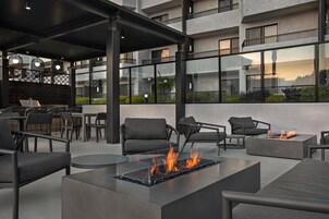 An outdoor seating area with modern furniture, a glass-top fire feature, and a view of a building with balconies.