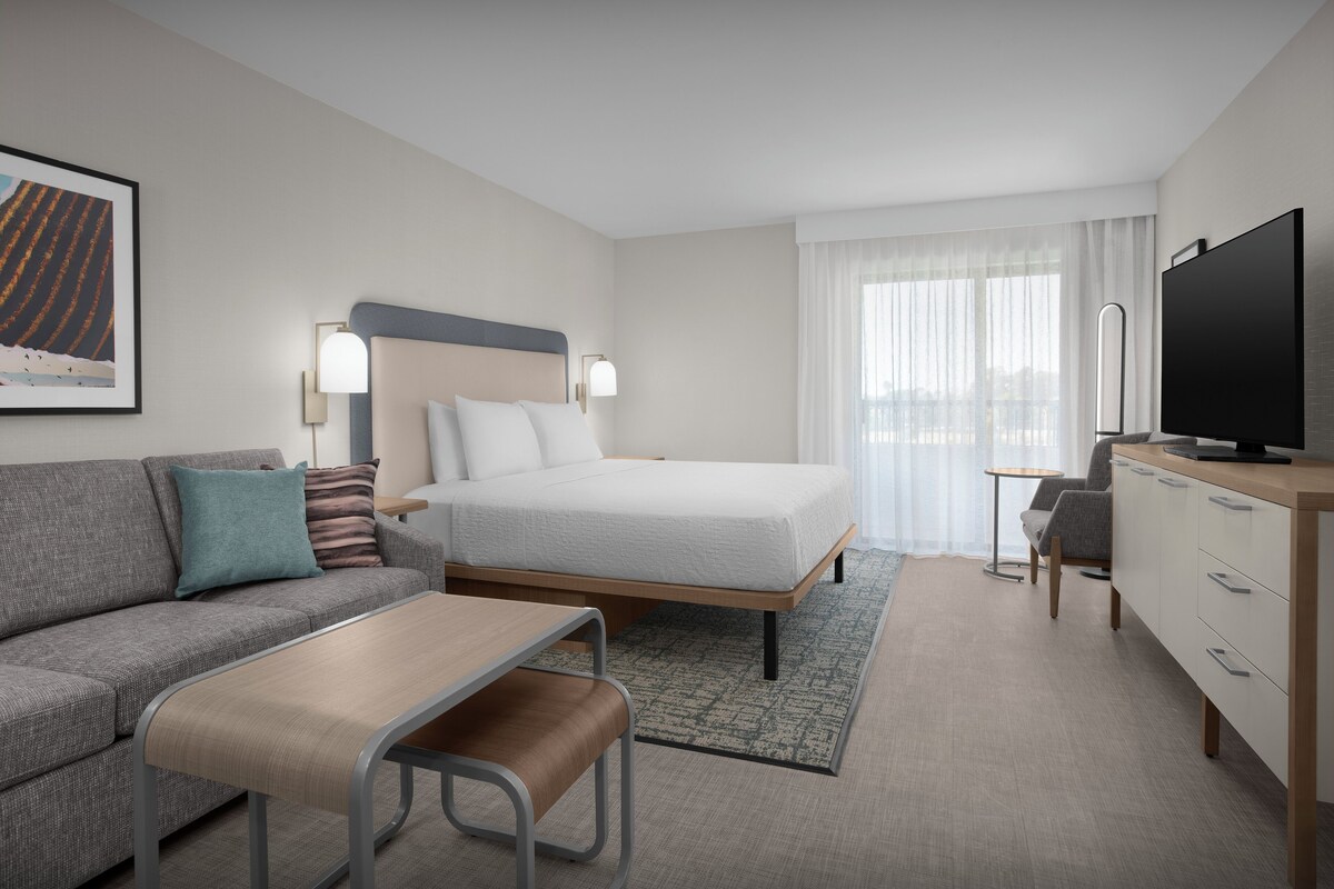 Ein modernes Hotelzimmer mit Bett, Sofa, Schreibtisch und Fernseher.