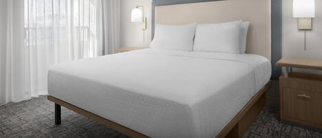 Una habitación de hotel con una cama grande, dos mesitas de noche y un ventanal con cortinas translúcidas.