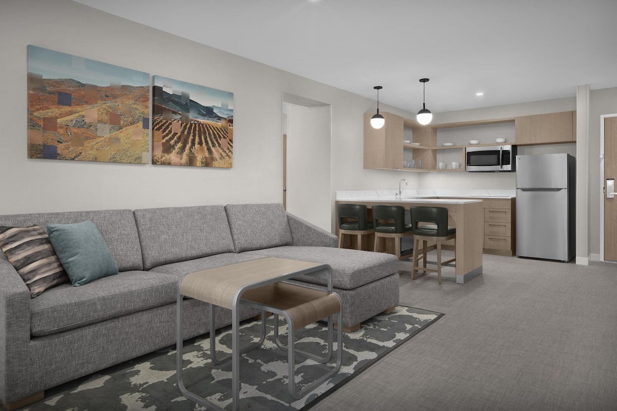 A modern kitchen with a built-in microwave and refrigerator, a grey sofa with a bench, and two pendant lights.