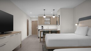 Una habitación de hotel moderna con una cama grande, un escritorio con silla, un televisor y una kitchenette.