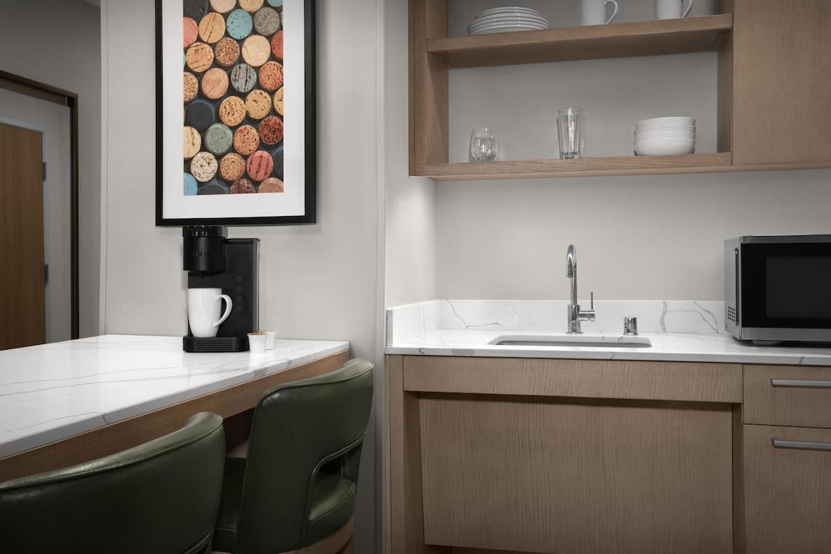 A modern kitchen with a coffee maker, sink, microwave, and a shelf with dishes.