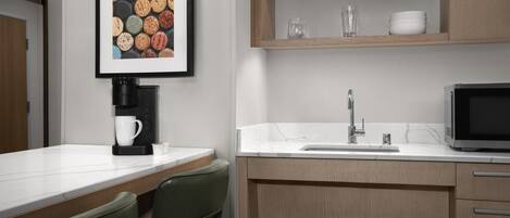 A modern kitchen with a coffee maker, sink, microwave, and a shelf with dishes.