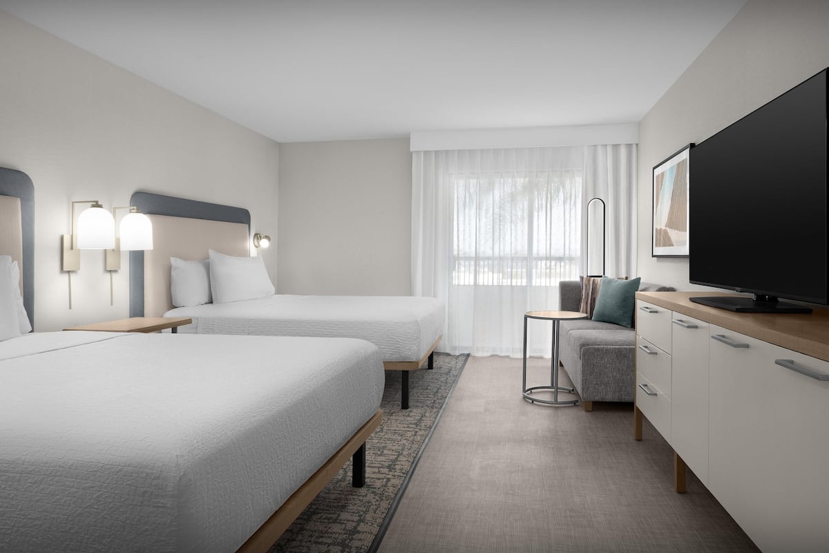 A hotel room with two beds, a TV, a desk, and a small seating area.