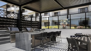 Un patio al aire libre con una parrilla, asientos y vistas a un edificio.