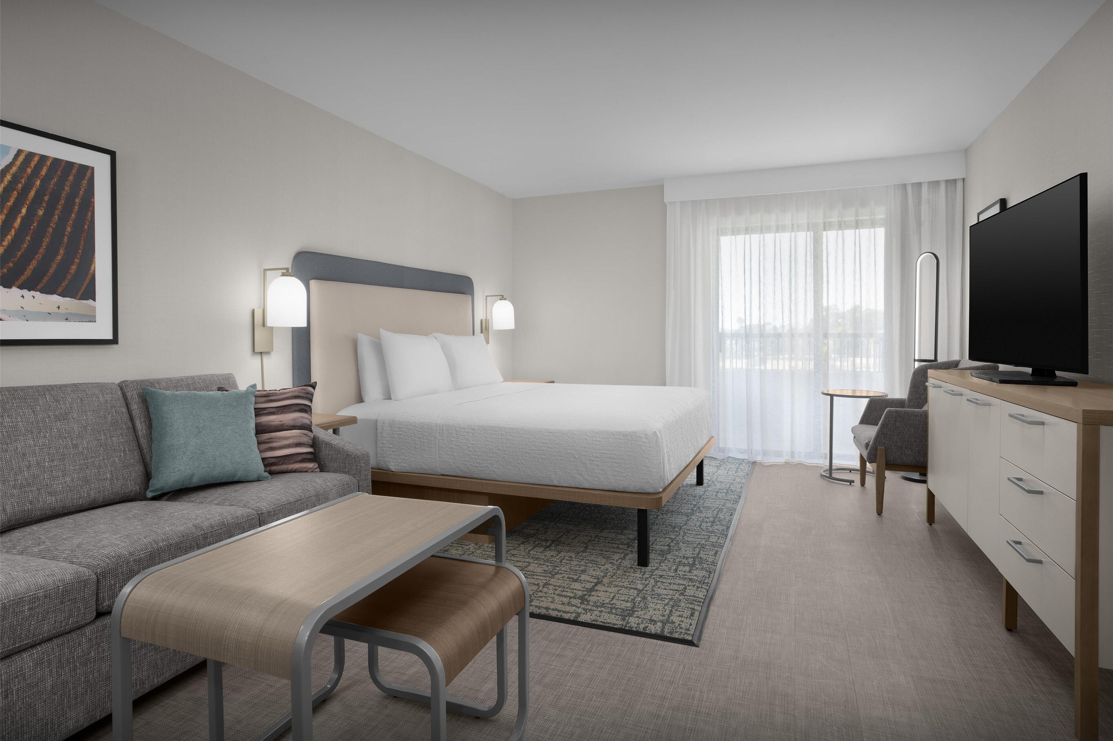 A hotel room with a bed, a sofa, a desk, a television, and a window with curtains.