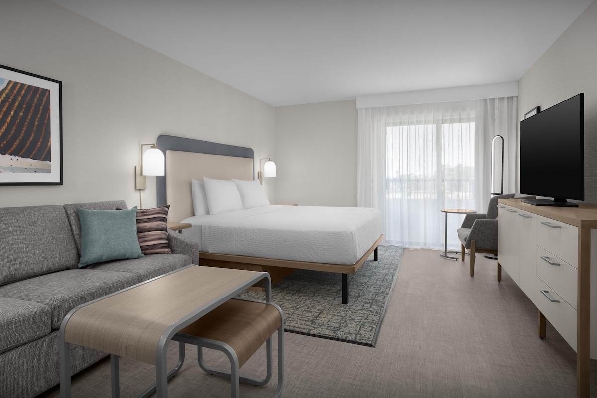 A hotel room with a bed, a sofa, a desk, a television, and a window with curtains.