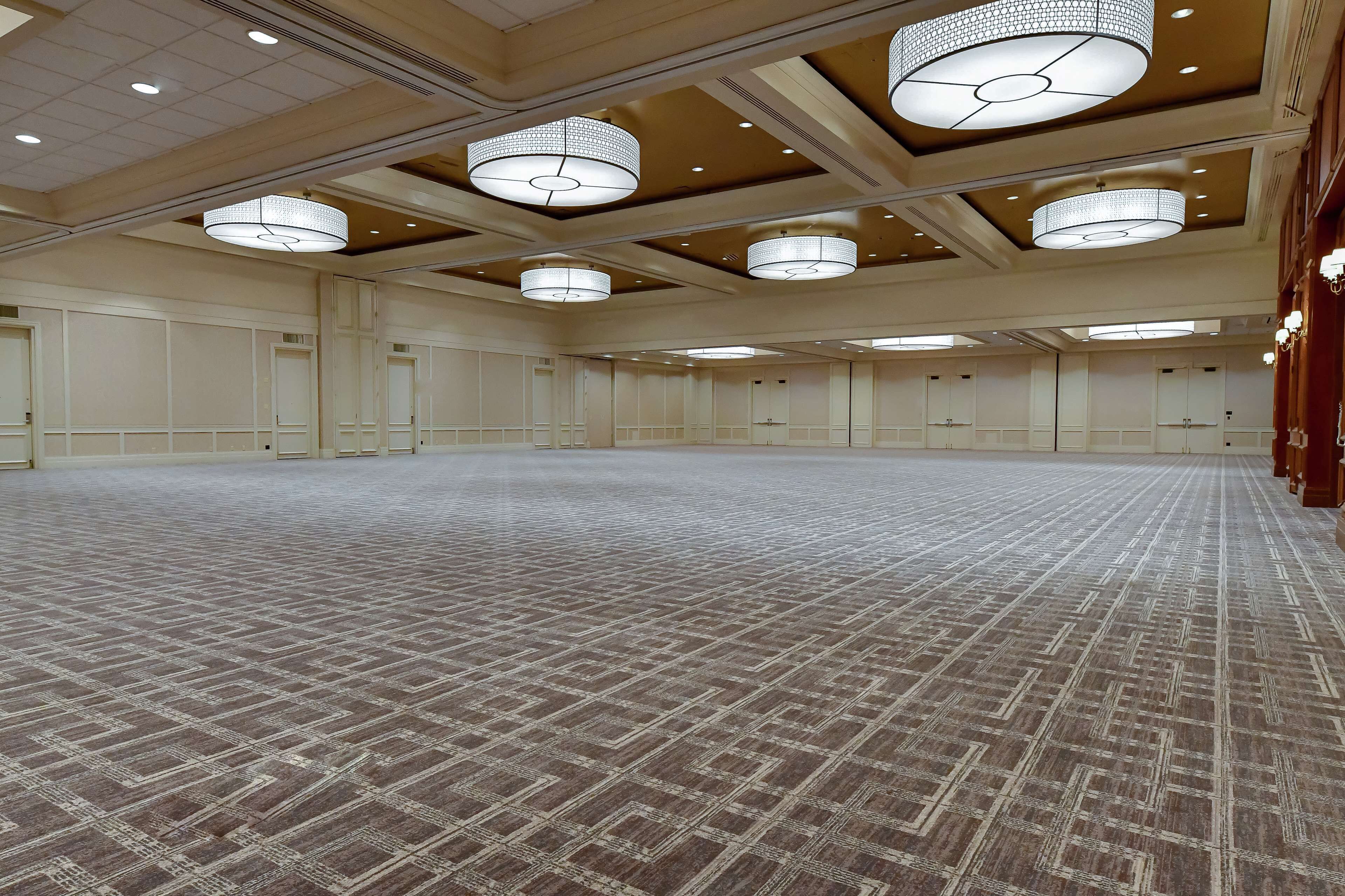 A spacious conference room with a patterned carpet, multiple doors, and large, circular chandeliers.