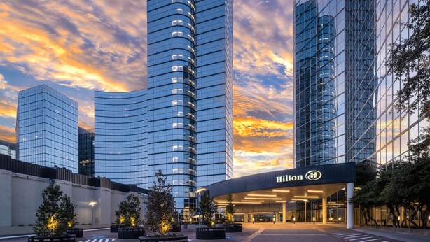 A modern hotel with a curved glass facade, a prominent entrance with the Hilton logo, and a landscaped courtyard with trees. - Hilton Dallas Lincoln Centre by the Galleria (Dallas)